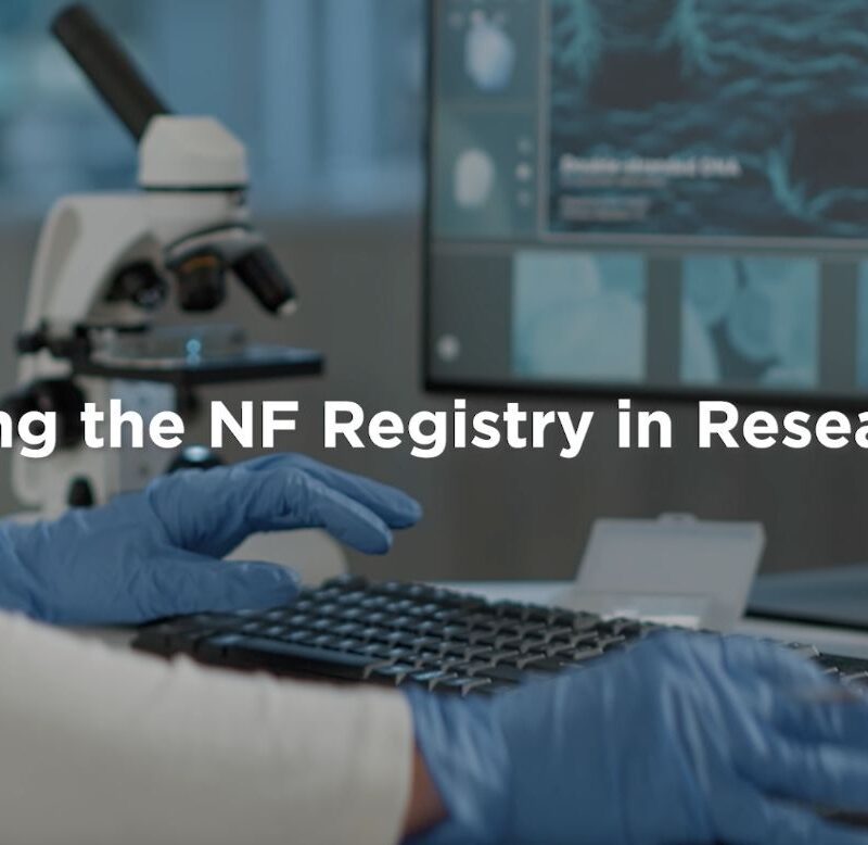 A researcher typing on a keyboard in a lab with a microscope and computer screens displaying cell images, titled "using the nf registry in research.