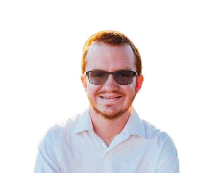 A man with glasses smiling, wearing a white shirt against a bright white background.