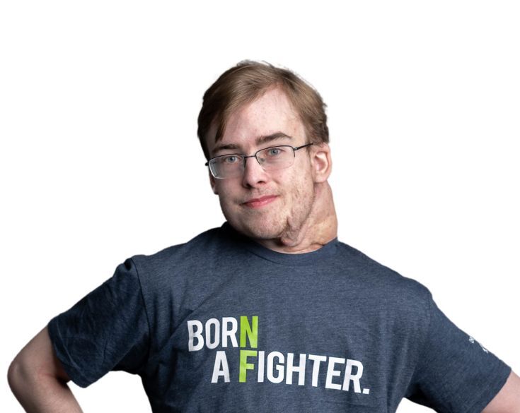 Man with light brown hair and glasses wearing a grey t-shirt that reads "born a fighter," smiling confidently, isolated on a white background.
