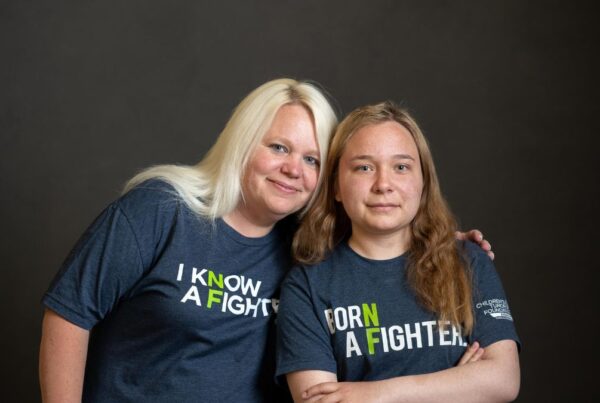 Two women, one blonde and one brunette, wearing t-shirts with motivational slogans, gently smiling against a dark background.