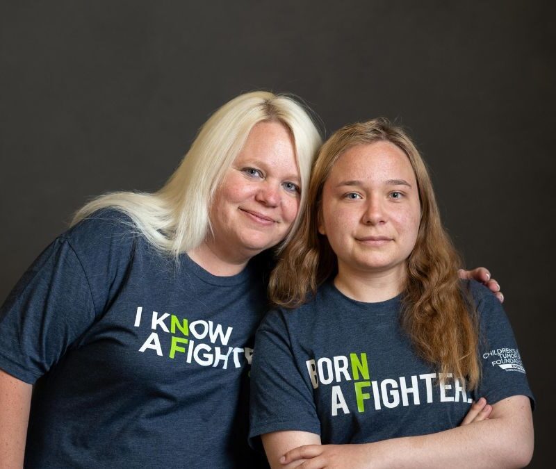 Two women, one blonde and one brunette, wearing t-shirts with motivational slogans, gently smiling against a dark background.