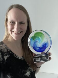 Woman smiling at the camera, holding an award with a colorful spiral design inside a glass sphere.