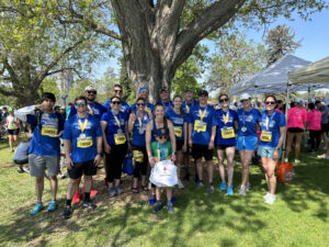 Group of joyful runners posing with medals under a tree at a park during a sunny day.