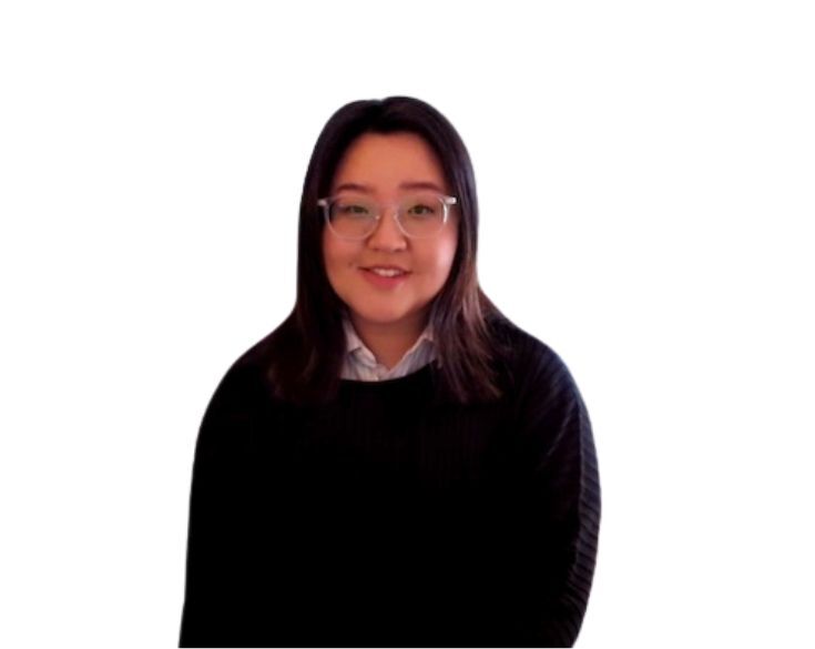 Young asian woman with glasses, wearing a dark sweater over a collared shirt, smiling gently against a light background.