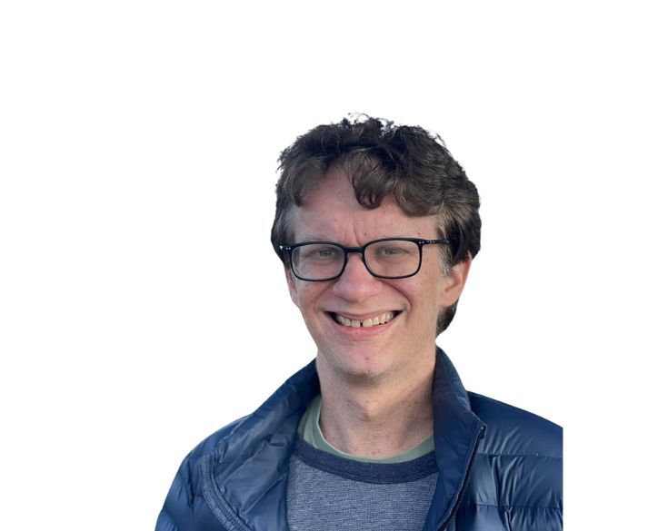 Smiling man with curly hair wearing glasses and a blue jacket against a white background.