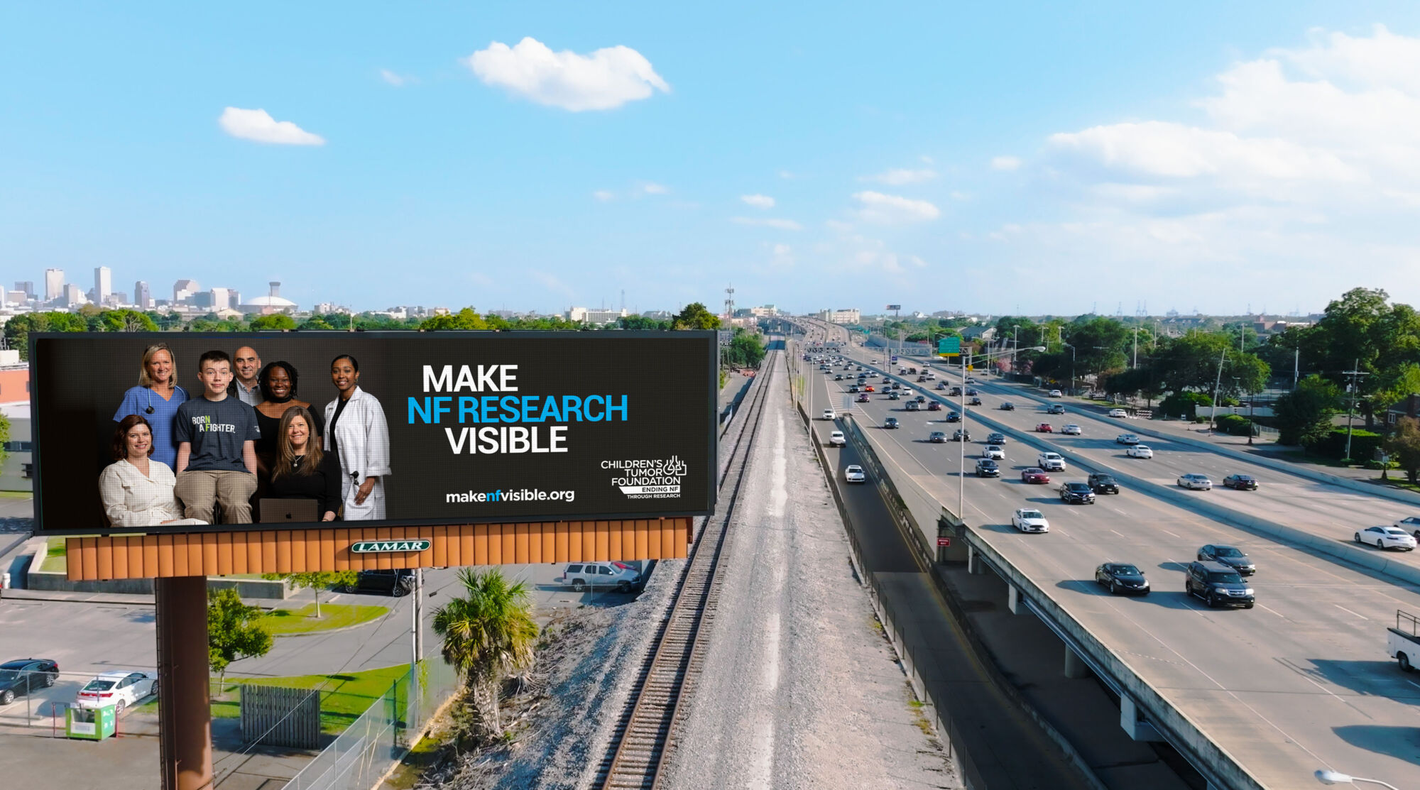 Billboard featuring a group of diverse people with the text "make nf research visible" beside a busy highway with city skyline in distance.