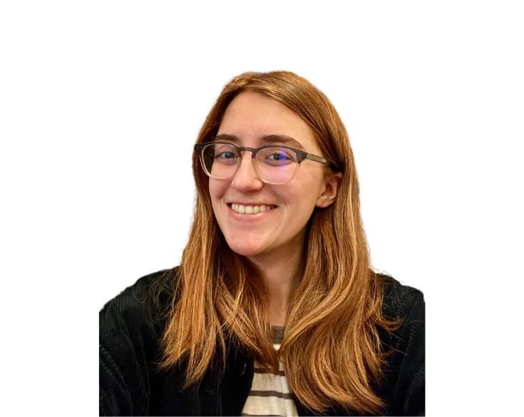 Smiling woman with long red hair and glasses, wearing a black jacket over a striped shirt, white background.