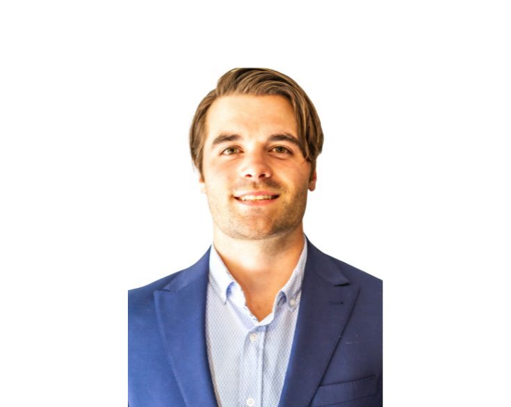 A man in a blue suit smiling against a white background.