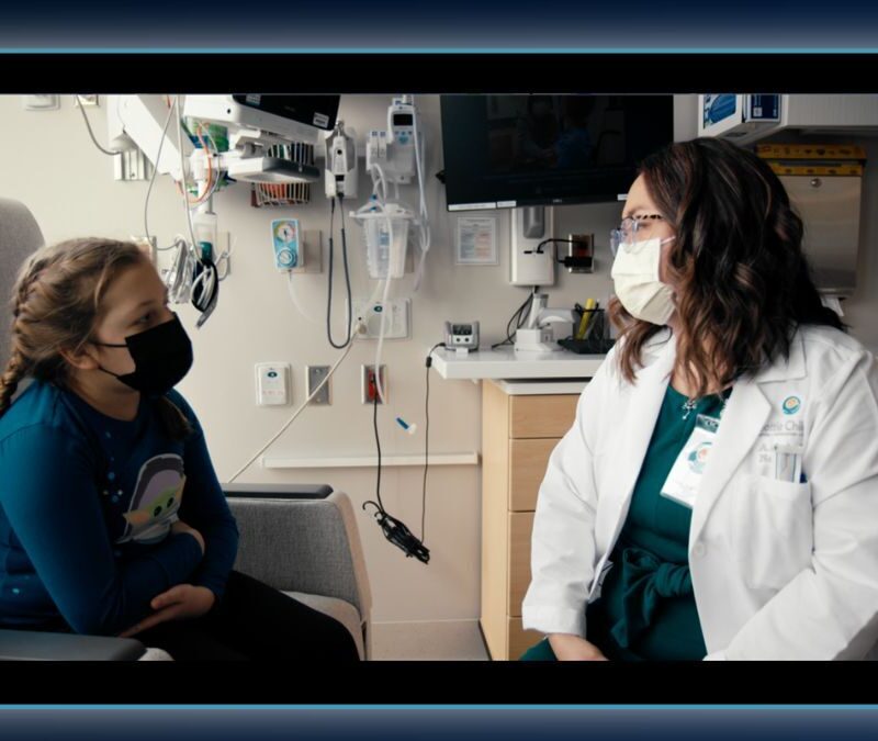 Healthcare professional in a white coat speaking with a young patient in a medical facility.