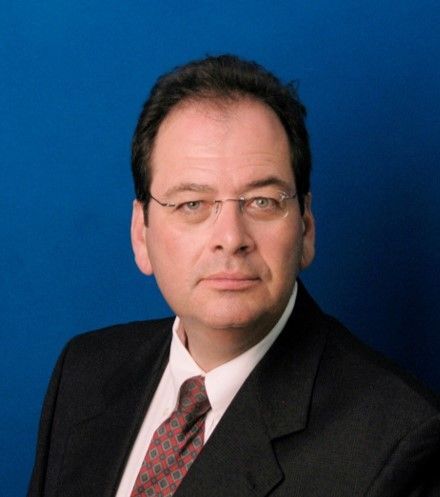 A person in a suit and tie is posing against a plain blue background.