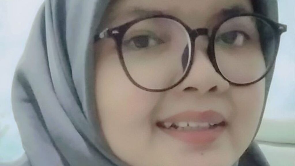 Person wearing glasses and a hijab, smiling at the camera.