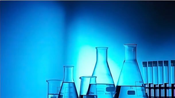 Several glass laboratory beakers, flasks, and test tubes filled with liquid are arranged against a blue-lit background.