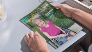 A person holds a magazine titled "NF News," featuring a smiling young girl in a pink shirt seated in a wheelchair on the cover.