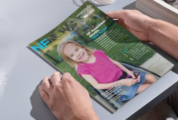 A person holds a magazine titled "NF News," featuring a smiling young girl in a pink shirt seated in a wheelchair on the cover.