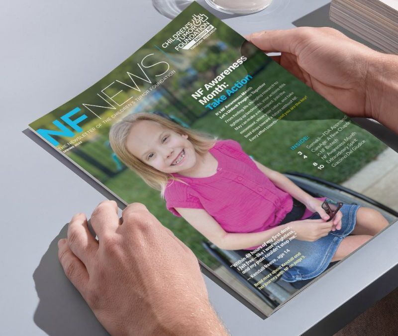 A person holds a magazine titled "NF News," featuring a smiling young girl in a pink shirt seated in a wheelchair on the cover.