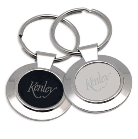 Two round metal keychains are shown, one with a black center and the other with a white center. Both have the word "Kenley" engraved on them.