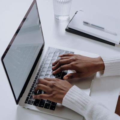 Person typing on a laptop with a notebook and a glass of water on the desk.
