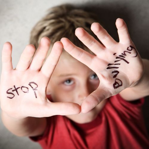 A child holds up hands with "stop bullying" written on the palms, looking up at the camera.